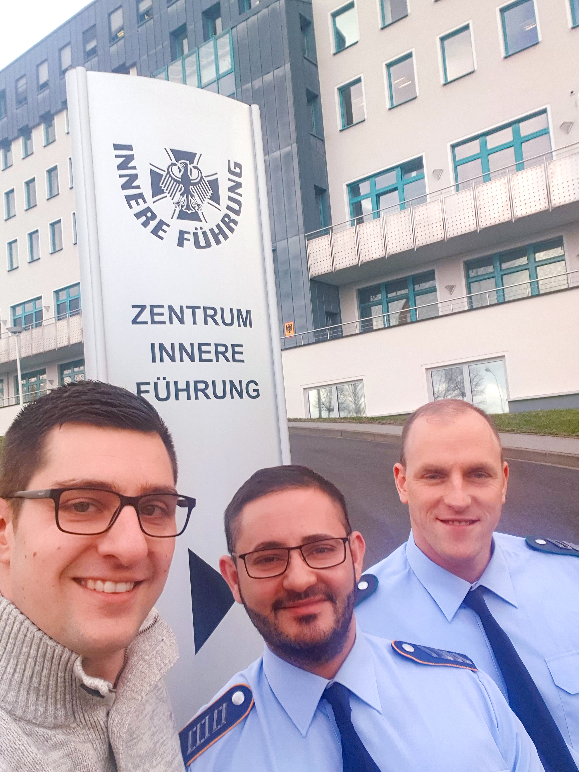 Drei Personen, eine zivil, zwei mlitärisch, vor dem Haupthaus des Zentrums Innere Führung.