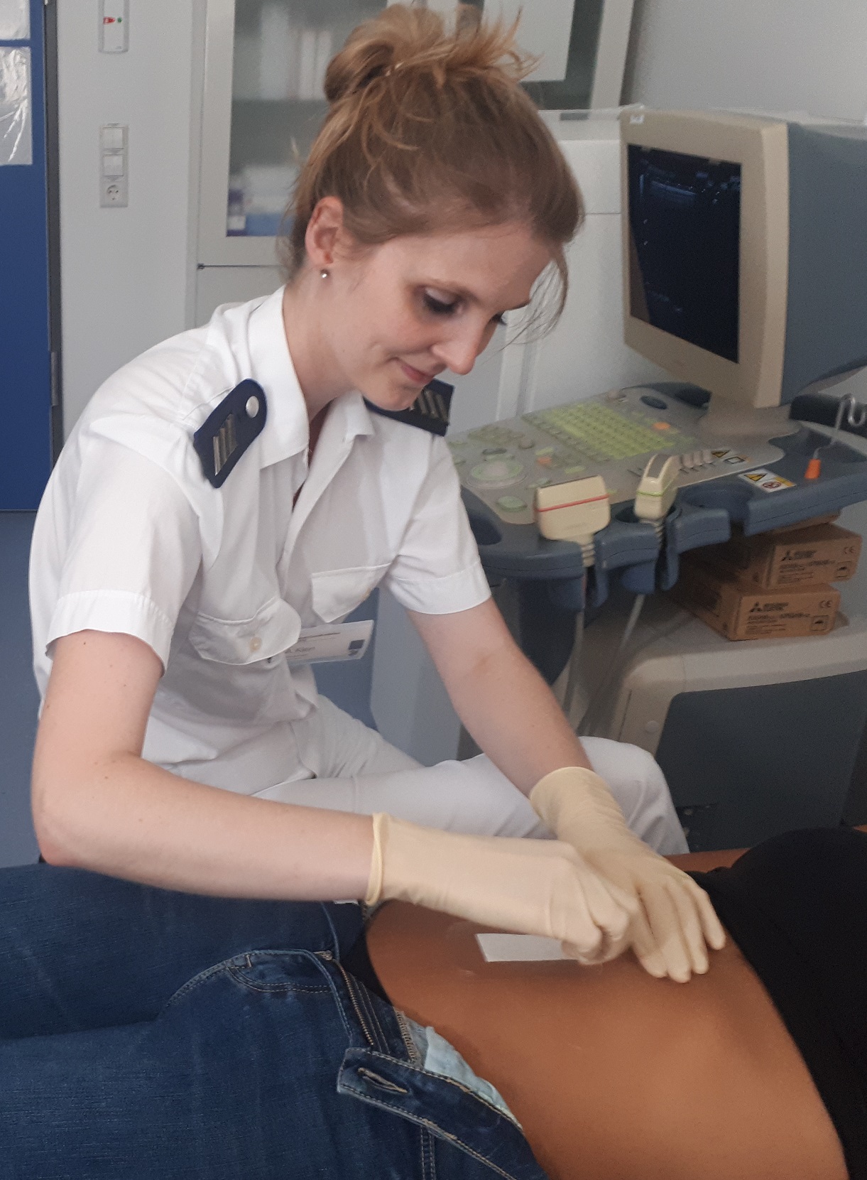 Eine Reservistin behandelt eine Patientin und löst ein Pflaster vom Bauch der Patientin.