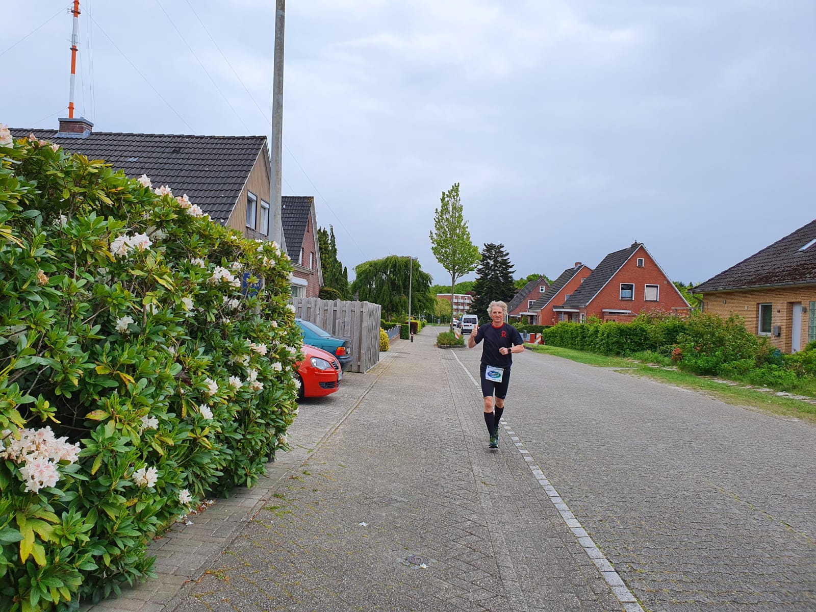 Laufsportler in kurzer dunkler Laufbekleidung beim Zieleinlauf in einem Wohngebiet.