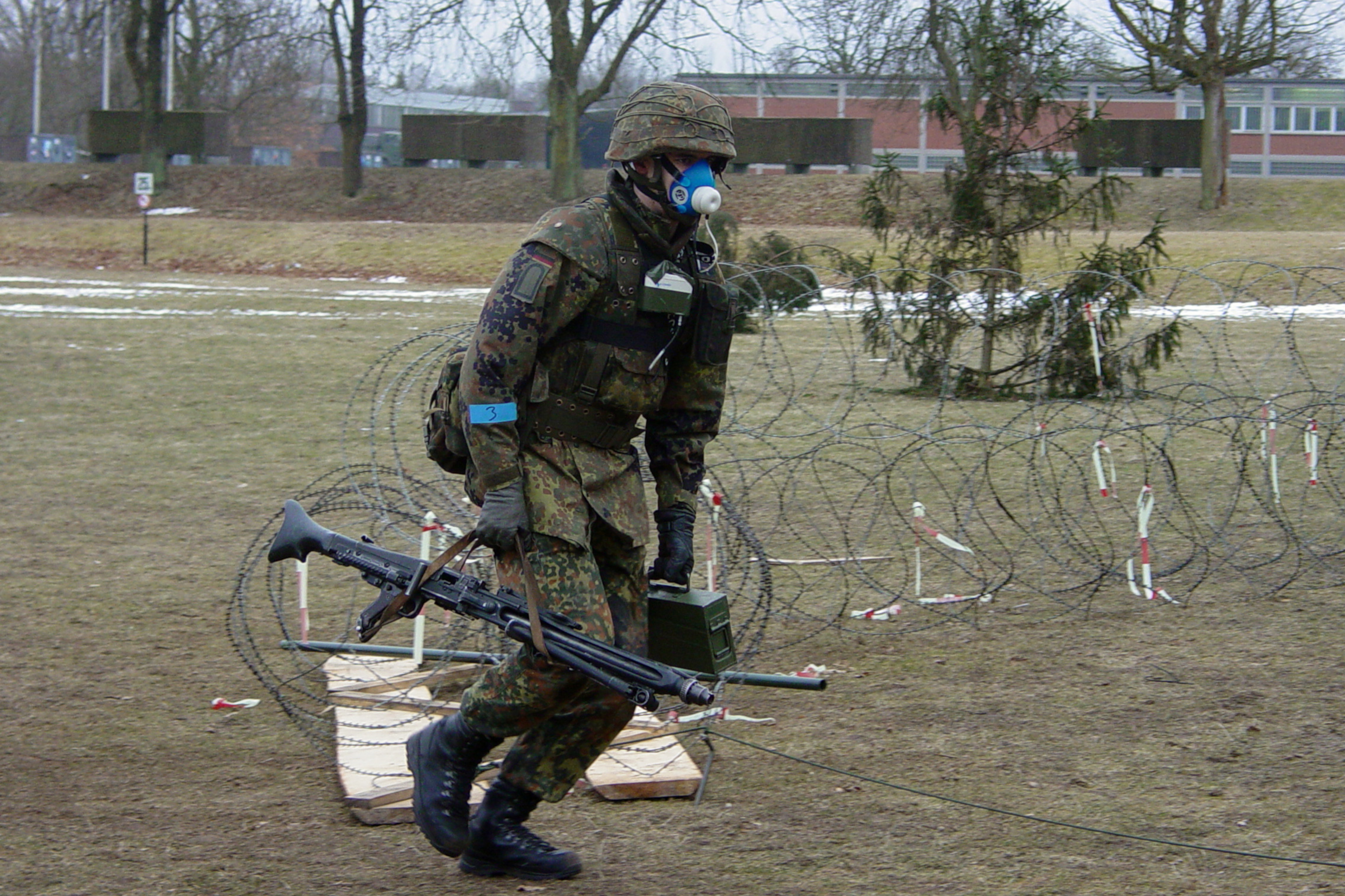 Soldier in full gear, machine gun in his right hand, metal box in his left, breathing mask, sensors attached to the body