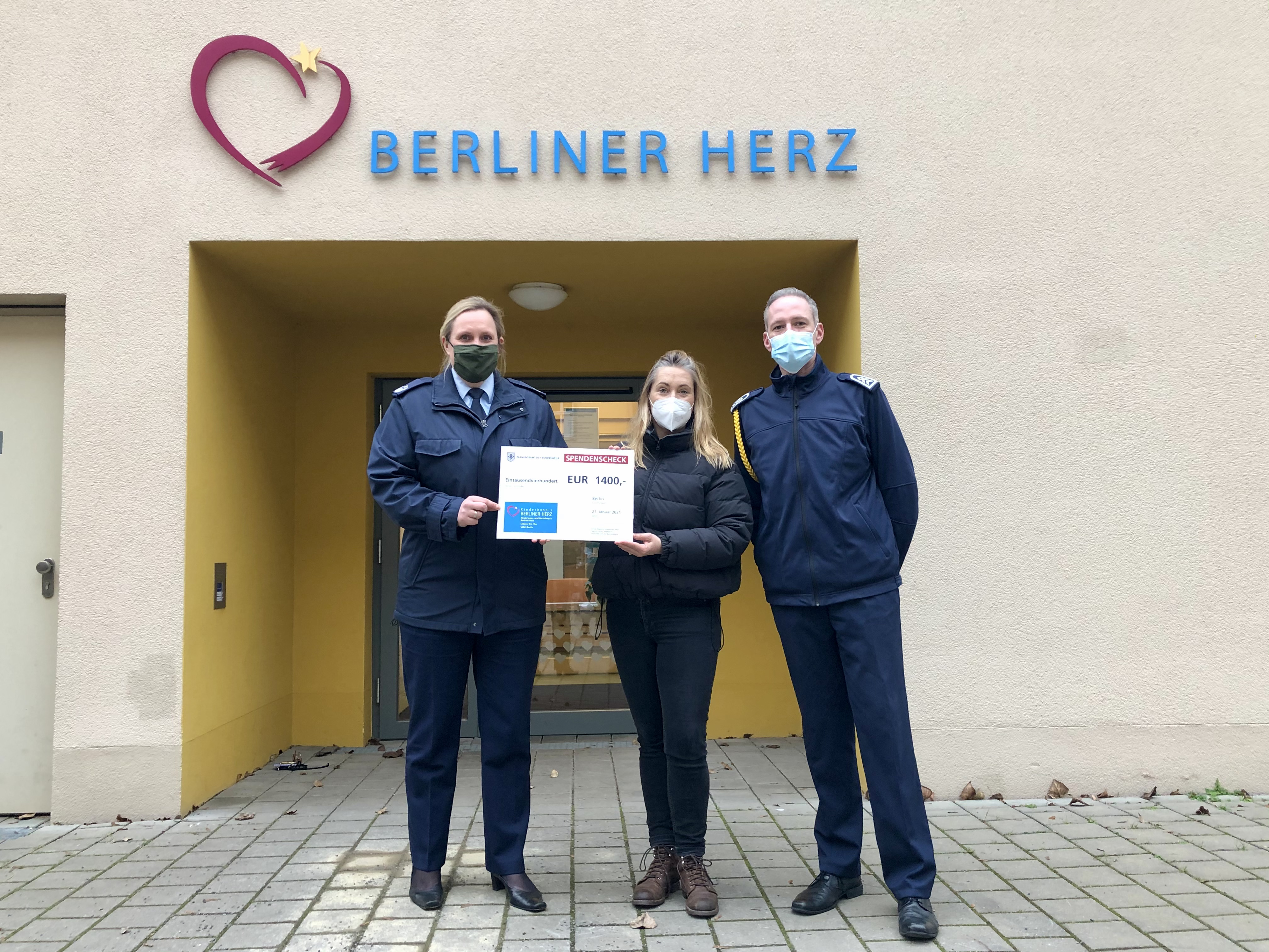 Soldatin und Soldat übergeben einen Scheck an eine Frau.