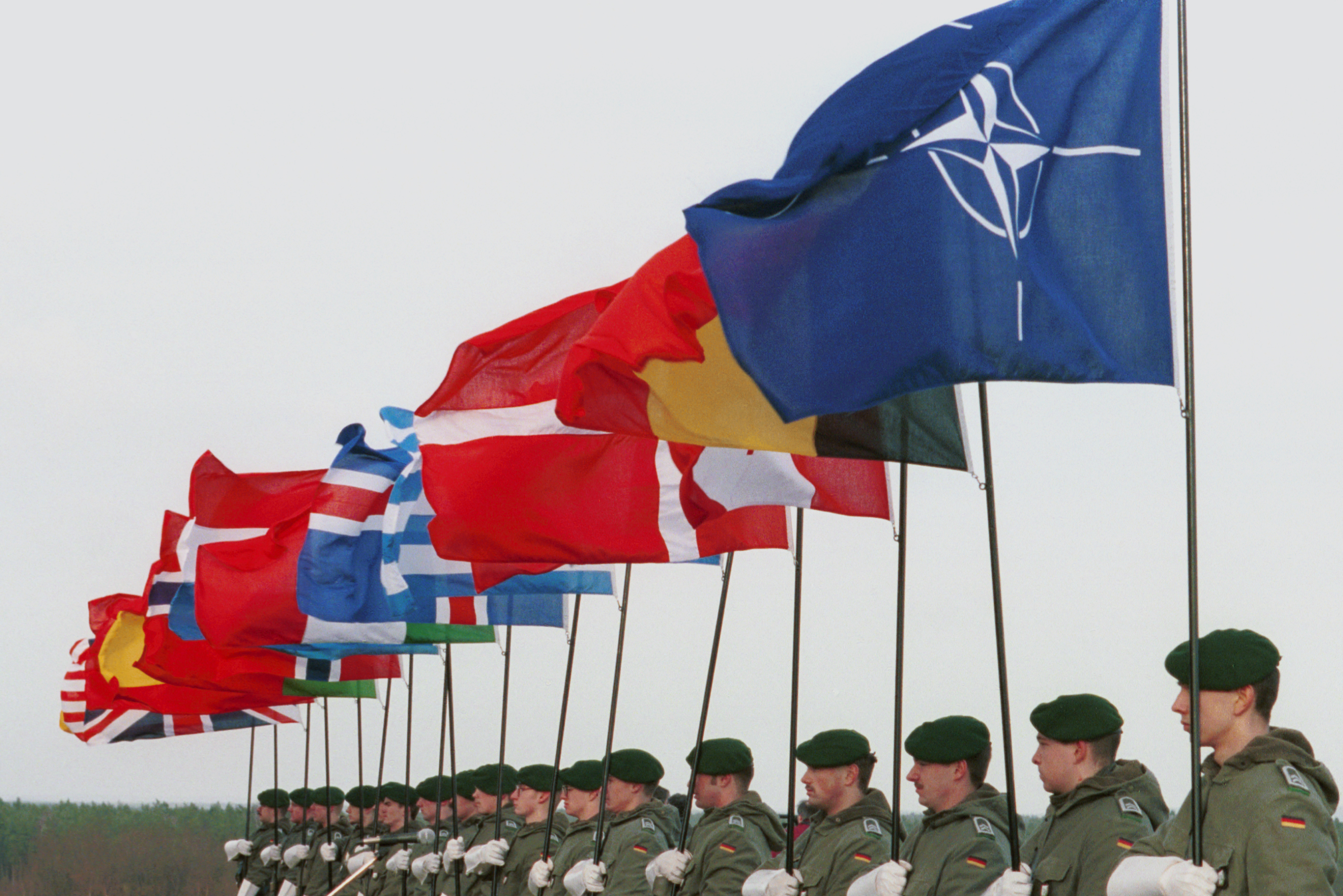 Die Flaggen der NATO-Mitgliedstaaten werden durch Soldaten gehalten.