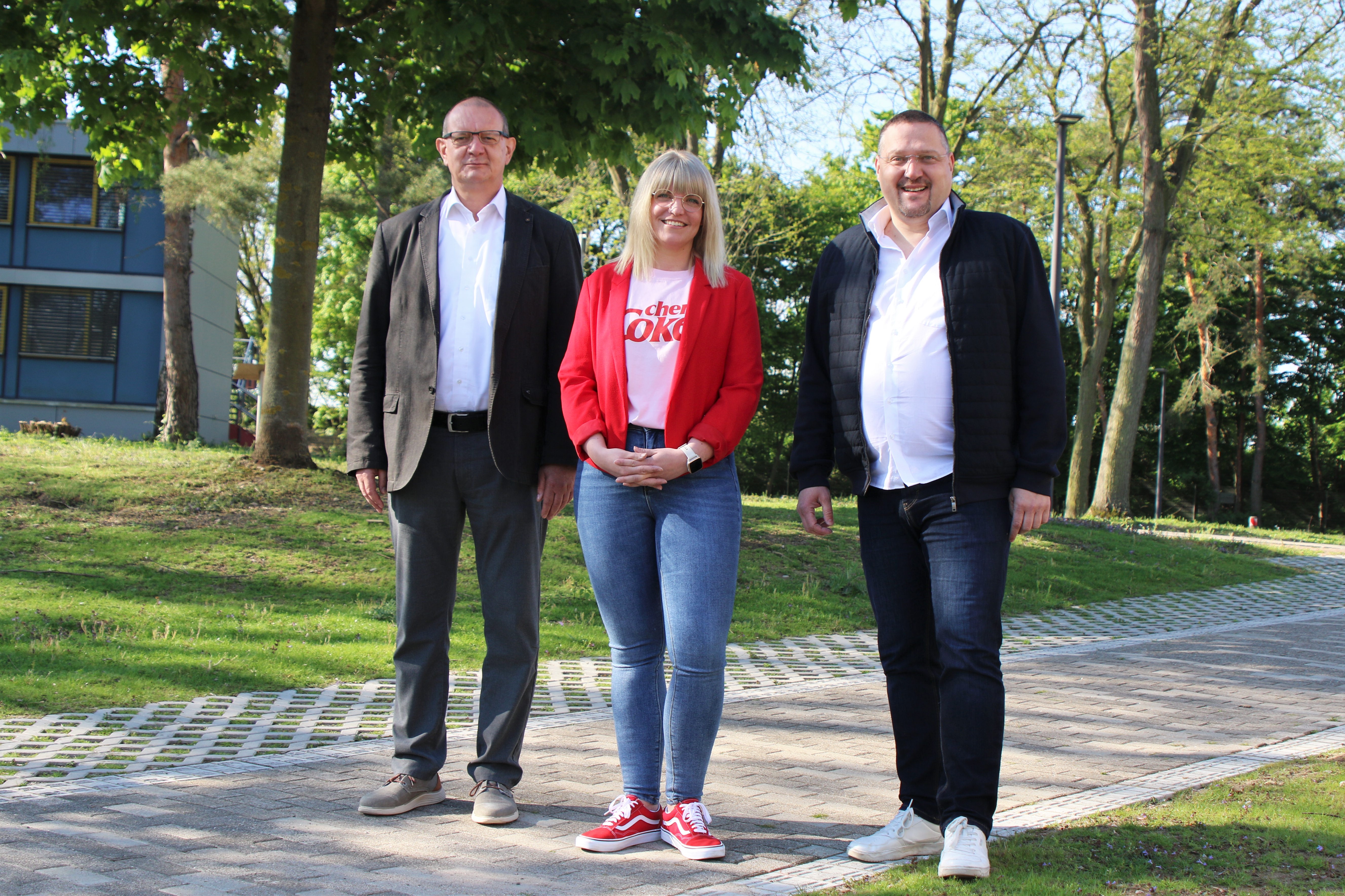 Zwei Männer und eine Frau stehen vor einem Gebäude.