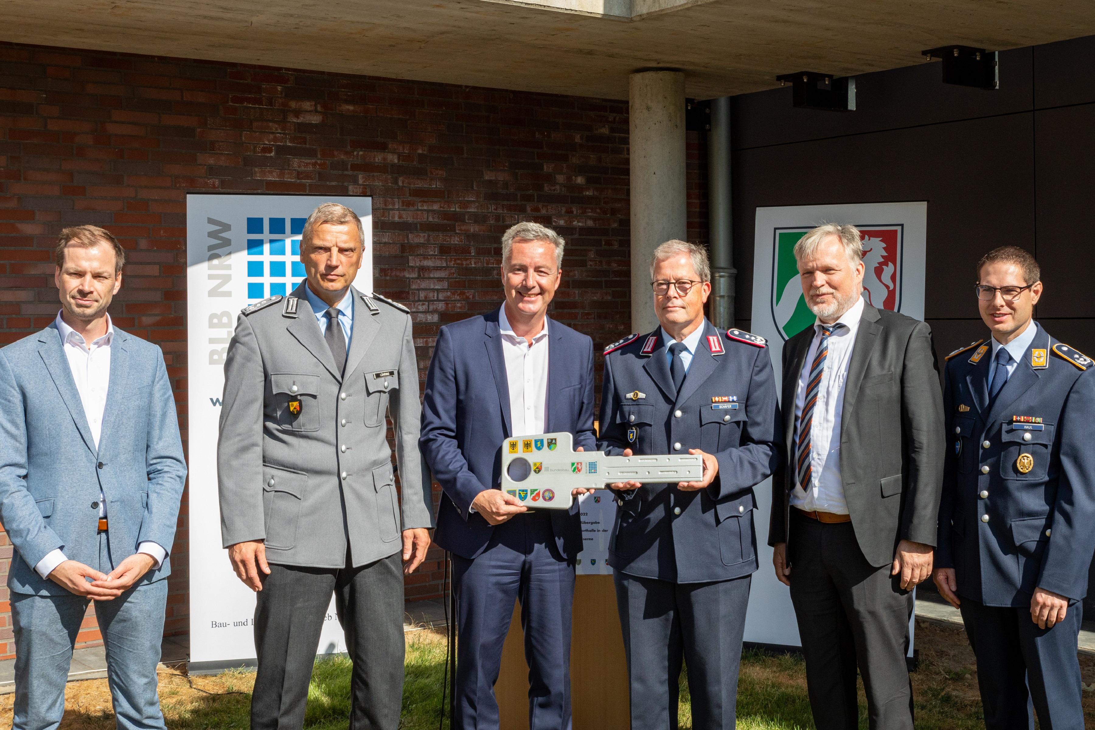 6 Männer in zivil und Uniform, ein symbolischer Schlüssel wird übergeben.