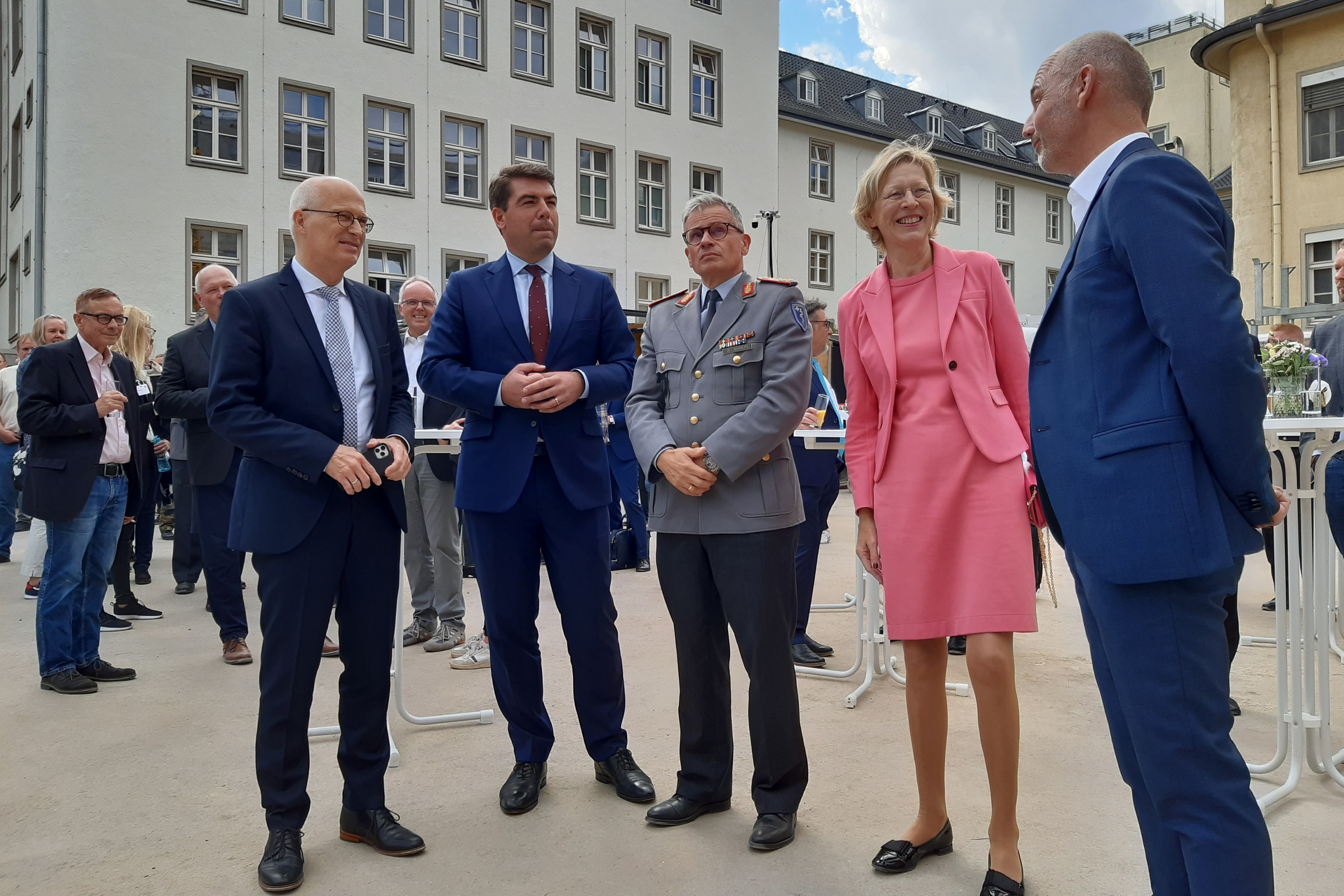 3 Herren in Anzug, ein General und eine Dame unterhalten sich