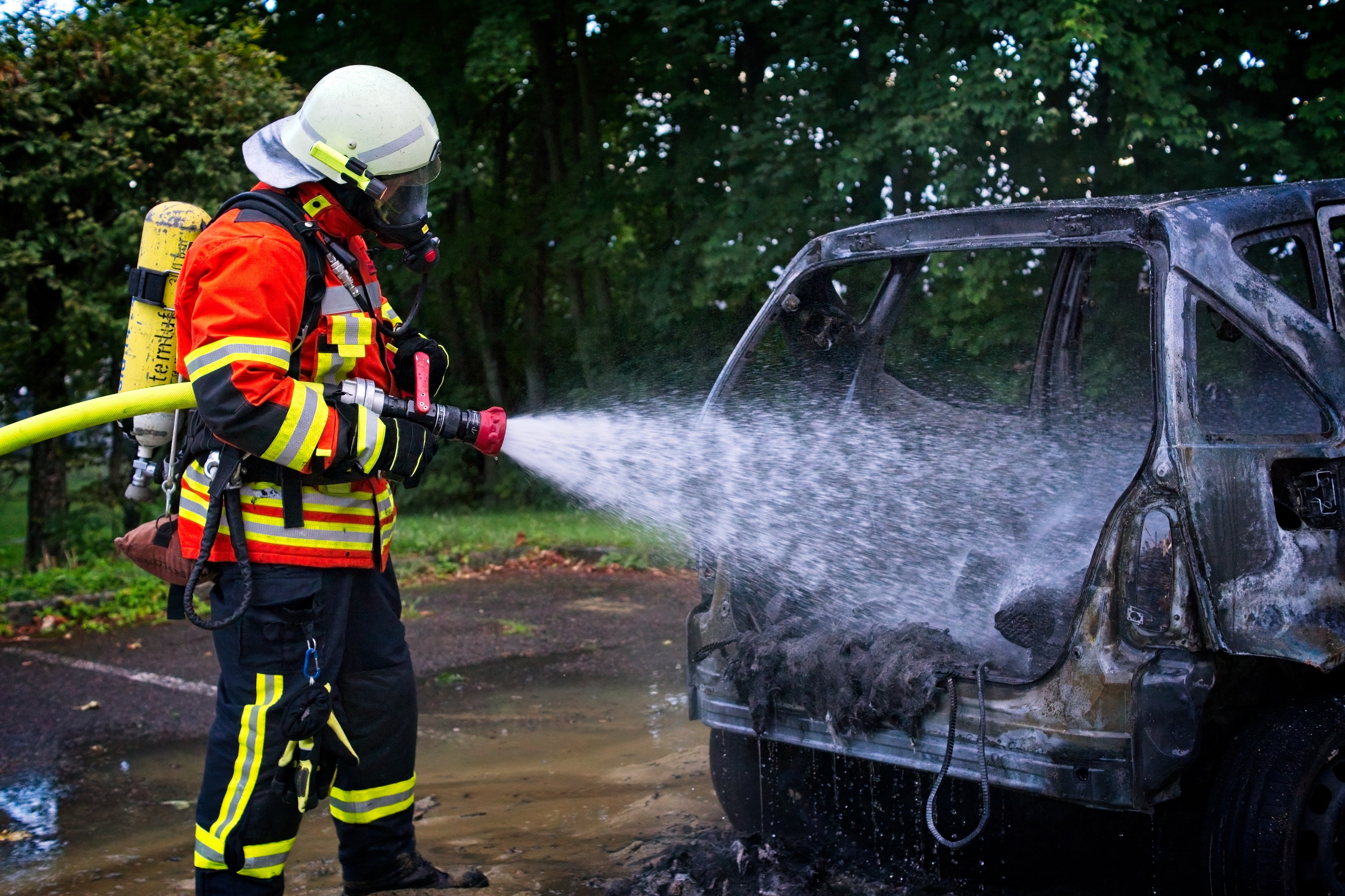 Ein Feuerwehrmann löscht die letzte Glut an einem ausgebrannten Fahrzeug