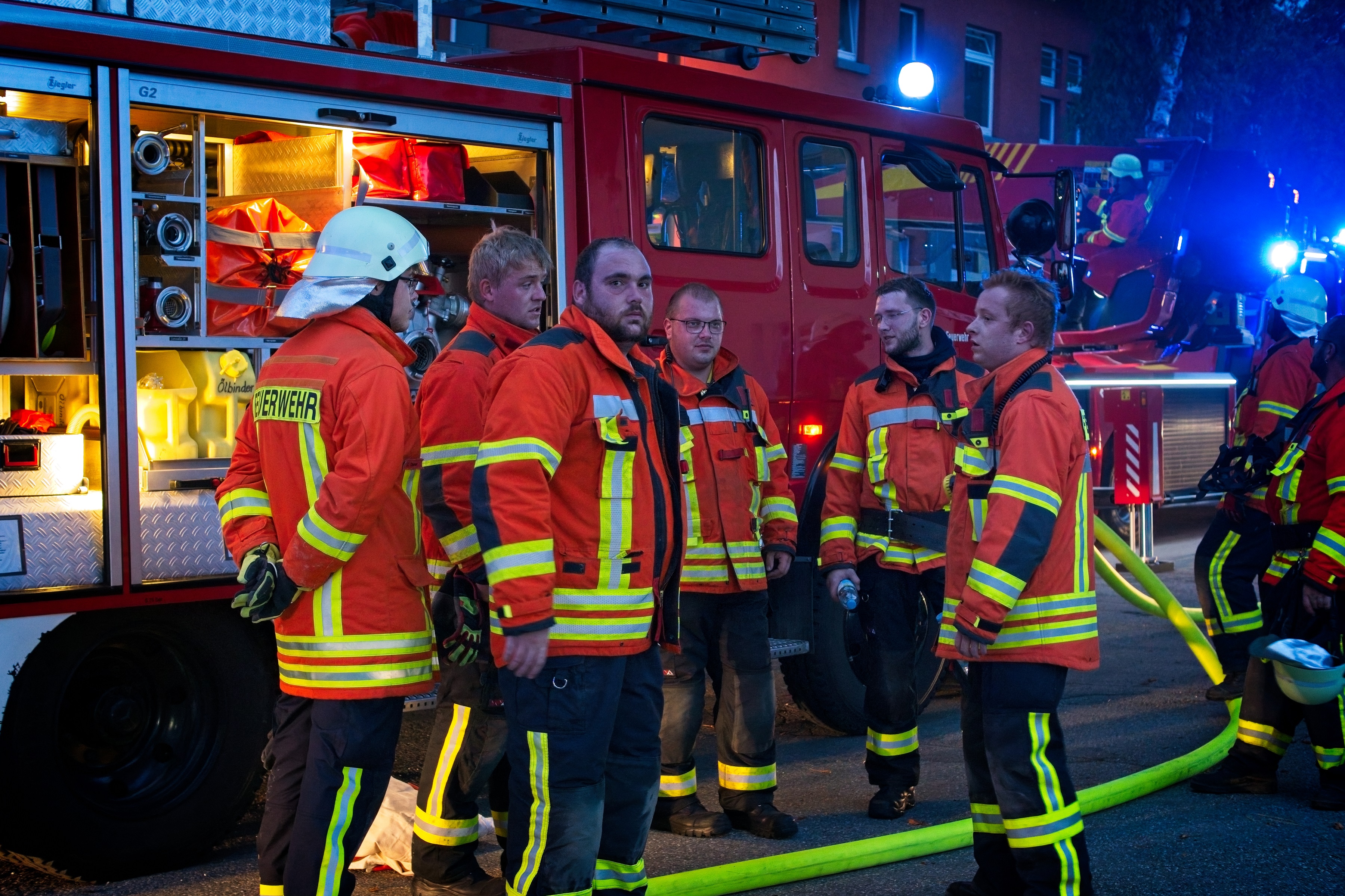 Mehrere erschöpfte Feuerwehrmänner stehen vor ihrem Feuerwehrfahrzeug