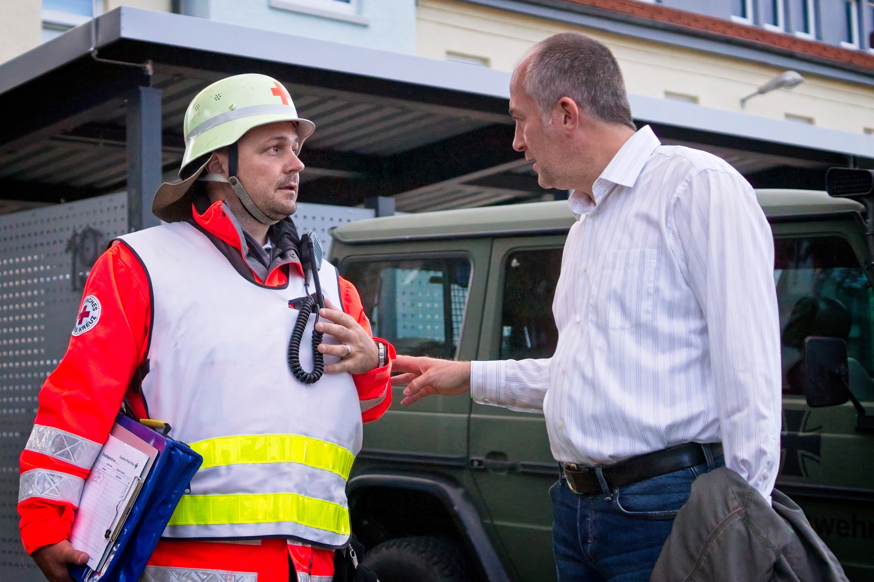 Ein zivil gekleideter Mann spricht mit einem Einsatzleiter des DRK in Rettungsuniform
