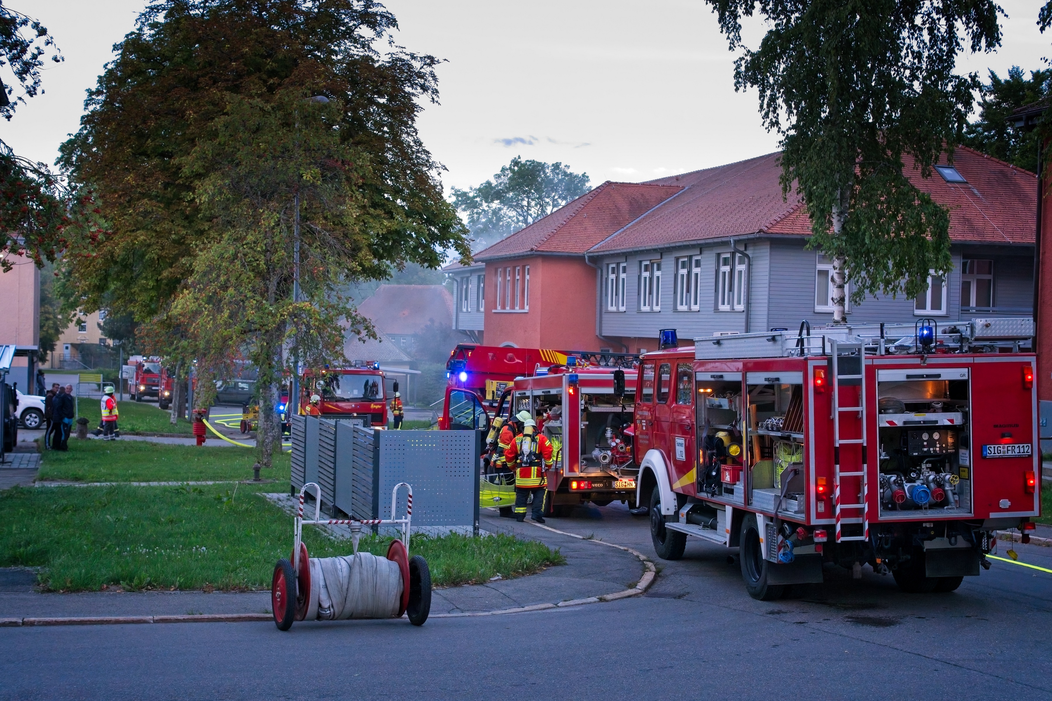 Feuerwehrfahrzeuge vor einem Gebäude, aus diesem dringt Rauch nach draußen