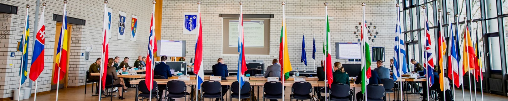 A large room with flags, soldiers sitting at tables in the background.