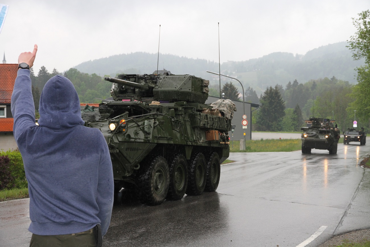 Panzer fahren hintereinander. Am Straßenrand steht ein Jugendlicher und hebt einen Arm.