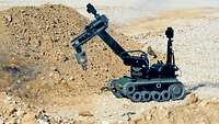 Der Roboter tEODor steht vor einem Sand- und Steinhaufen und beseitigt ein Kampfmittel