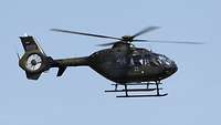 Ein Hubschrauber vom Typ EC 135 fliegt vor blauem Himmel in großer Höhe.