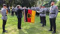 Ein Politiker befestigt an einer Truppenfahne, die ein Soldat hält, das Fahnenband.
