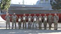 Soldaten sind mit der Urkunde in der Hand vor einem Schiff angetreten