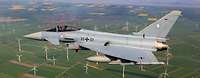 Ein Kampfflugzeug Eurofighter der Bundeswehr über einem Windpark.