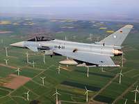 Ein Kampfflugzeug Eurofighter der Bundeswehr über einem Windpark.
