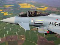 Ein Kampfflugzeug Eurofighter der Bundeswehr fliegt über einen Windpark.