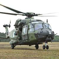 Ein Mehrzweckhubschrauber NH-90 schwebt mit einem aus der Seitentür herausschauenden Soldaten über dem Boden.