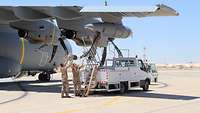 Unter einem Flügel des A400M arbeiten drei Soldaten und ziehen den Betankungsschlauch aus dem Behälter