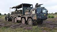 In der Heide: Drei Soldaten bedienen das Minenverlegesystem 85, ein Soldat sichert vom Lkw aus bewaffnet den Vorgang.