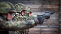 Drei Soldaten stehen auf einer Schießbahn nebeneinander und zielen jeweils mit einer Pistole auf Zielscheiben.