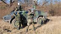 Drei Soldaten befinden sich neben und auf einem Spähwagen Fennek. Der vordere Soldat startet eine Drohne.