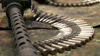 Ein Patronengurt mit Munition liegt neben der Mündung eines Maschinengewehrs.