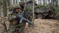 Zwei Soldaten in einem Wald knien mit dem Gewehr G36 in den Händen neben einem Schützenpanzer