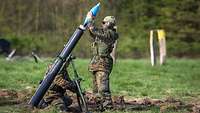 Zwei Soldaten befinden sich an einem Mörser. Einer zielt, der andere belädt die Waffe mit Munition.