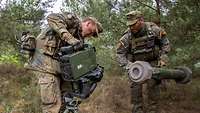 Zwei Soldaten bauen ein Panzerabwehrsystem in einem Waldstück auf. 