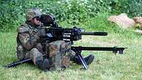 Ein Soldat sitzt in einem Wald hinter einer Granatmaschinenwaffe und schaut durch das Visier