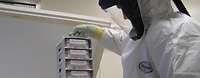 Ein Mitarbeiter in einem weißen Schutzanzug hält tiefgefrorene Proben in der Hand.