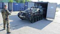Ein Soldat weist ein kleines Kettenfahrzeug ein, das rückwärts in einen Transportcontainer fährt.
