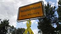 Ortschild mit der Aufschrift „Veitshöchheim – Kreis Würzburg“, darunter eine Gelbe Schleife
