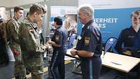 Ein Polizist spricht mit einem Soldaten an einem Informationsstand.