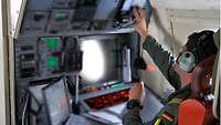 Ein Soldat sitzt im Flugzeug und bedient verschiedene Elemente