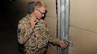 Ein Soldat leuchtet mit einer Taschenlampe auf ein Vorhängeschloss an einem Tor