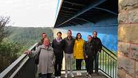 Gruppe junger Mensch auf einer Plattform, im Hintergrund eine Autobahnbrücke
