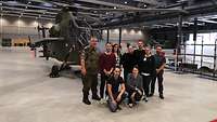  Gruppenbild mit rund 10 Personen vor einem Kampfhubschrauber in einem Hangar