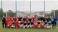 Gruppenfoto beider Mannschaften vor einem Fußballtor, einige hocken und einige stehen dahinter.