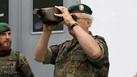 Ein Soldat hält mit beiden Händen einen Laserentfernungsmesser schaut durch.