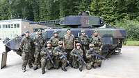 Eine Gruppe von zehn Soldaten steht und hockt bewaffnet vor dem Schützenpanzer Puma.