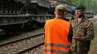 Zwei Soldaten im Gespräch, im Hintergrund mehrere Panzer verladen auf Eisenbahnwagen