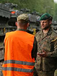 Zwei Soldaten im Gespräch, im Hintergrund mehrere Panzer verladen auf Eisenbahnwagen