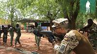 Ein deutscher Ausbilder steht mit der Waffe im Anschlag vor den malischen Soldaten