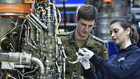 Ein Soldat und eine Mitarbeiterin der Firma MTU Aero Engines begutachten gemeinsam ein Triebwerk-Bauteil.