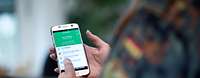 Coach PTBS App Eine Hand in Uniform tippt auf einem Smarphone, auf dem die PTBS-App angezeigt wird