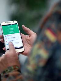 Eine Hand in Uniform tippt auf einem Smarphone, auf dem die PTBS-App angezeigt wird