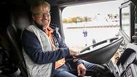 Ein Mann am Lenkrad eines Lkws, die Türen der Fahrerkabine sind geöffnet und er lächelt.